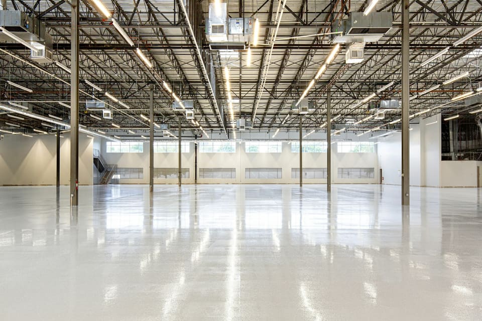 Kontraktova Depot — a vast empty industrial hall with an exposed steel-truss ceiling, clerestory daylight and a seamless resin floor, ready for adaptive reuse.