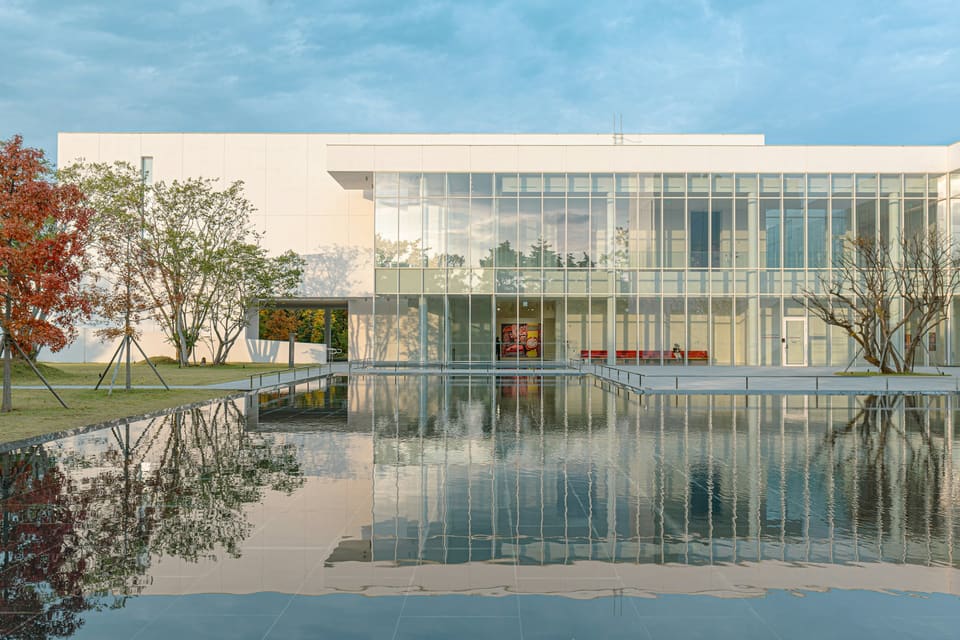 Obolon Reflection — a long white gallery building with a full-height glazed facade mirrored in a still reflecting pool.
