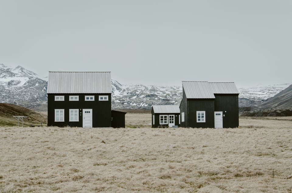 Verkhovyna Retreat — a pair of black timber-clad cabins with pale metal roofs in a highland meadow beneath snow-dusted mountains.