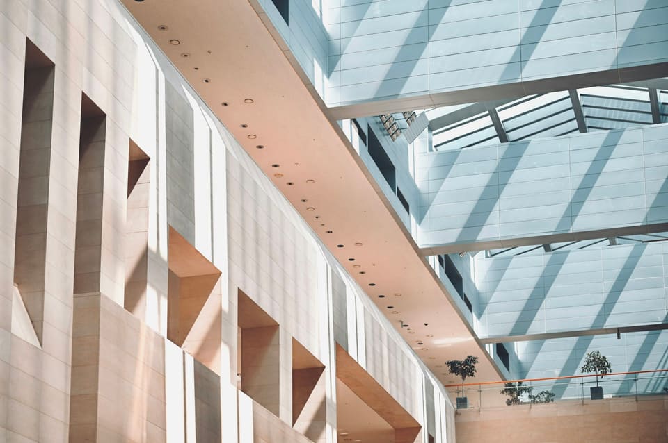 Pechersk Atrium — a soaring cultural atrium where a glazed roof casts diagonal daylight across a stone wall carved with deep triangular recesses.